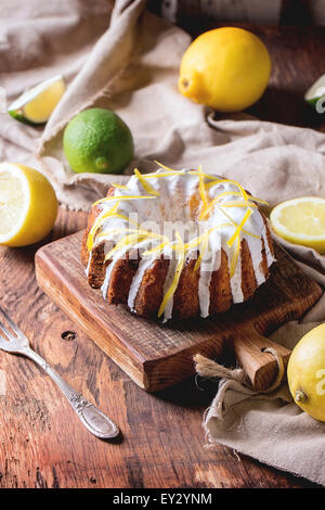 Torte con glassa bianca e la scorza di limone, servita con limoni e lime sul piccolo taglio di legno pannelli in legno backgr Foto Stock