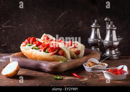 In casa hot dogs sul piatto di legno con ingredienti di senape e salsa di pomodoro, cipolla, peperoncino, rosmarino sul tavolo di legno. Rustico scuro s Foto Stock