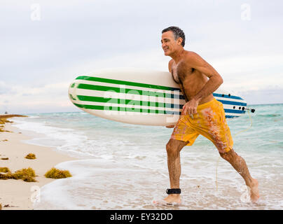 Medium shot di un senior in esecuzione fuori dall'acqua dopo aver terminato la sua sessione di navigazione Foto Stock
