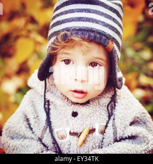 Close-up ritratto di Carino curioso Toddler Boy con grandi occhi in maglia striata Hat cercando in autunno Park. Kid Holding coni. Foto Stock