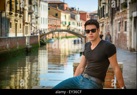 Ritratto di attraente dai capelli scuri Giovane appoggiata contro la ringhiera a piedi ponte sullo stretto canale a Venezia, Italia Foto Stock