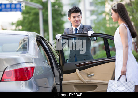 Chauffeur apertura porta auto per una giovane donna Foto Stock