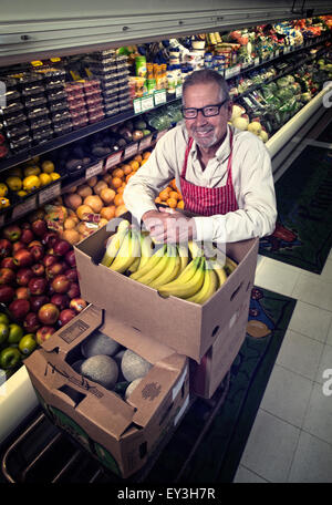 Un uomo in piedi in un negozio di alimentari accanto a un display di frutta fresca e verdura. Foto Stock