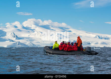 Gruppo di persone che attraversano l'Oceano Antartico in una barca di gomma, le montagne ricoperte di neve in background. Foto Stock