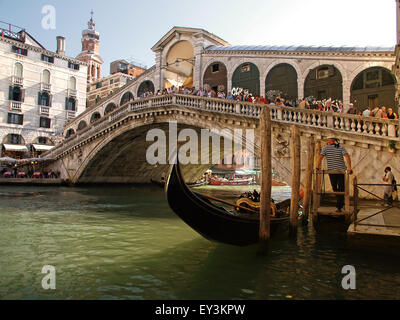 Gondola nero ormeggiato sotto il ponte di Rialto con il gondoliere in attesa per il turista a Venezia. L'Italia. Foto Stock