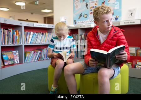 Yong un ragazzo e una ragazza la lettura nella sezione per bambini di una biblioteca pubblica Foto Stock