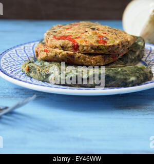 Primo piano di alcune differenti materie veggie hamburger in una piastra su un rustico in legno di colore blu nella tabella Foto Stock