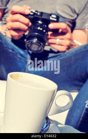 Primo piano di un giovane uomo nel controllo della sua fotocamera mentre egli es prendendo un caffè nella terrazza di un bar Foto Stock