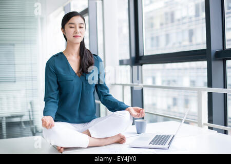 Giovane imprenditrice fare yoga sulla scrivania in ufficio Foto Stock