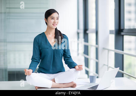 Giovane imprenditrice fare yoga sulla scrivania in ufficio Foto Stock