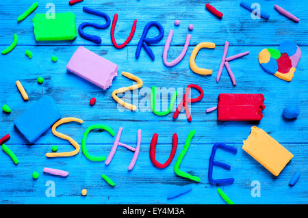 La frase zuruck zur schule, torna a scuola in tedesco, scritto con argilla di modellazione di diversi colori su un blu woode rustico Foto Stock