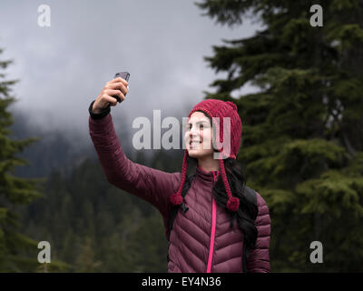 Vicino la foto di una sorridente donna caucasica tenendo selfie sulla montagna Foto Stock