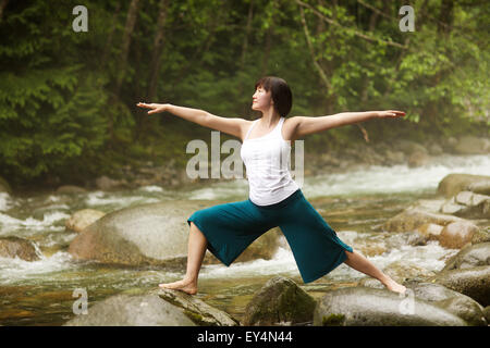 Donna asiatica di eseguire la posizione del Guerriero II pone yoga (Virabhadrasana) dal fiume, Lynn Valley, British Columbia, Canada Foto Stock