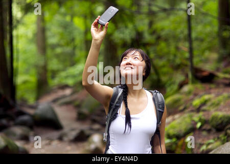 Donna asiatica di scattare foto indossando un zaino nero in una foresta Foto Stock