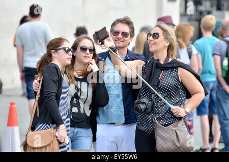 Londra, Inghilterra, Regno Unito. Gruppo di amici in Trafalgar Square di scattare una foto con un bastone selfie Foto Stock