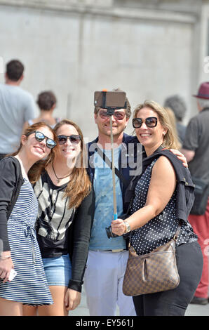 Londra, Inghilterra, Regno Unito. Gruppo di amici in Trafalgar Square di scattare una foto con un bastone selfie Foto Stock