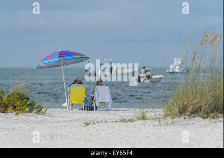 Due persone sedute su una spiaggia a guardare le barche dei pescatori in Boca Grande, Gasparilla Island, Florida, Stati Uniti d'America. Foto Stock