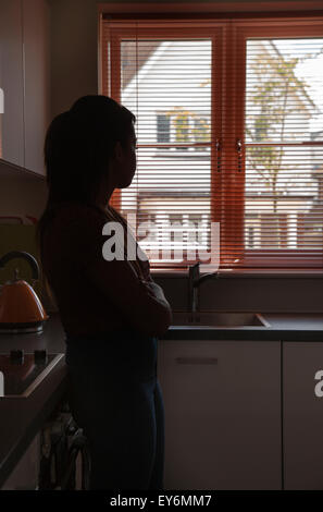 Silhouette di una giovane donna di guardare attraverso una finestra cieco, punto di vista posteriore. Foto Stock