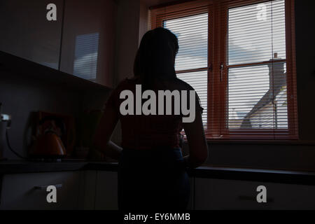 Silhouette di una giovane donna di guardare attraverso una finestra cieco, punto di vista posteriore. Foto Stock