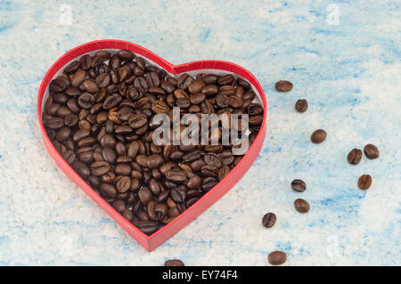 A forma di cuore scatola riempita con fried i chicchi di caffè su sfondo blu Foto Stock