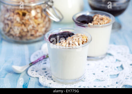 Due piccoli vasetti di yogurt fatto in casa con la marmellata di ribes nero e granola (semi di girasole, mais, avena e orzo in fiocchi e dadi) Foto Stock