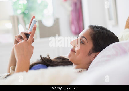 Ragazza adolescente (14-15) texting in camera da letto Foto Stock