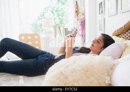 Ragazza adolescente (14-15) texting in camera da letto Foto Stock