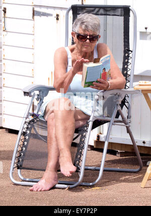 Vecchia donna seduto in una sedia a sdraio in spiaggia a leggere un libro con occhiali da sole sopra gli occhiali da lettura, Goodrington Sands Paignton, Devon Foto Stock