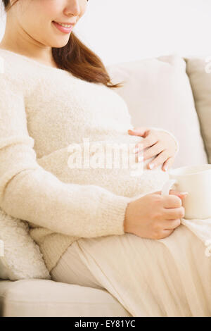Un giovane giapponese donna incinta sul divano Foto Stock