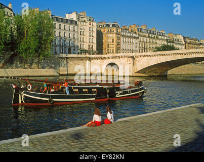 Due donne rilassante vicino a Ile St Louis sul Fiume Senna con la barca passando sotto edifici di appartamenti in Parigi Foto Stock