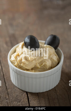 Cremosa di hummus con le olive in un recipiente piccolo sul tavolo di legno Foto Stock