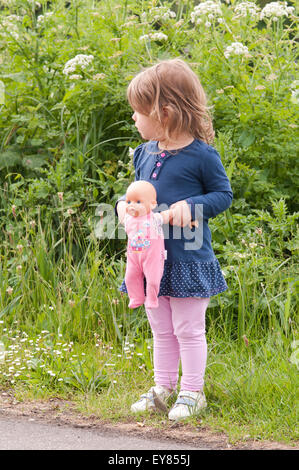 Bambina in piedi sul percorso che guarda lontano tenendo la bambola Foto Stock