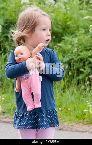 Bambina che guarda lontano cuddling sua bambola Foto Stock