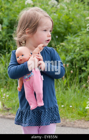 Bambina che guarda lontano cuddling sua bambola Foto Stock