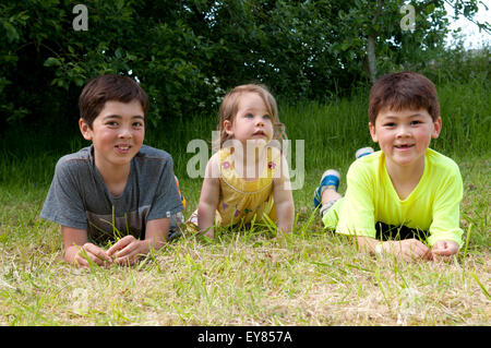 Bambina sdraiati sull'erba con due ragazzi Foto Stock