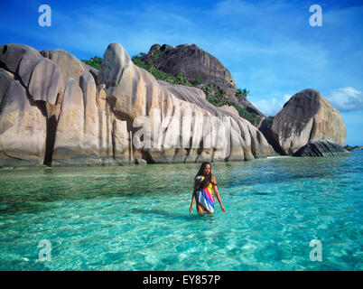 Donna nativa con colorati sarong camminare in acque aqua ad Anse Source d Argent su La Digue alle Seychelles Foto Stock