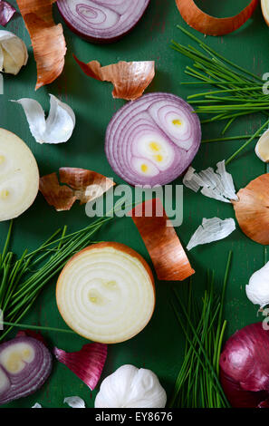 Cipolle, erba cipollina e aglio sparsi sul vecchio legno verde tabella per la preparazione del cibo e il concetto di cucina a vista. Foto Stock