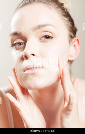 Giovane donna di applicare la lozione sul viso, close-up Foto Stock