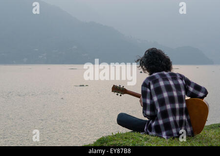 Un giovane uomo riproduce una chitarra sul lago Phewa, Pokhara, Nepal Foto Stock