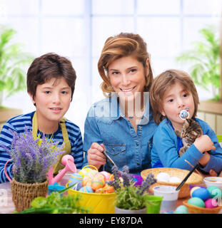 La famiglia felice la colorazione di uova, madre di due figli piccoli vernice tradizionali uova di Pasqua in diversi colori a casa Foto Stock