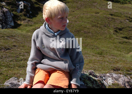 Ragazzo seduto sulla roccia che guarda lontano Foto Stock