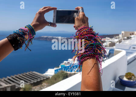 Un gran numero di braccialetti donna lavorato a maglia su quella della ragazza Mani UNA donna che prende una foto telefono Santorini paesaggio Grecia bracciali colorati di amicizia Foto Stock