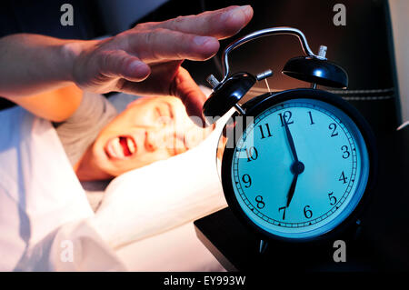 Giovane uomo caucasico nel letto sbadigli mentre si arresta la sveglia alle 7 di mattina Foto Stock