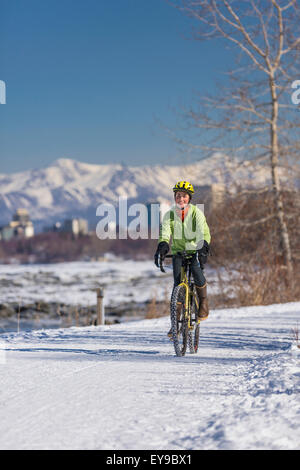 Una giovane donna corse pneumatici chiodati In bicicletta lungo il Percorso Costiero di Tony Knowles, Anchorage, centromeridionale Alaska, Stati Uniti d'America. Foto Stock