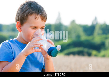 Boy utilizzando un inalatore per asma in villaggio con estate tramonto Foto Stock