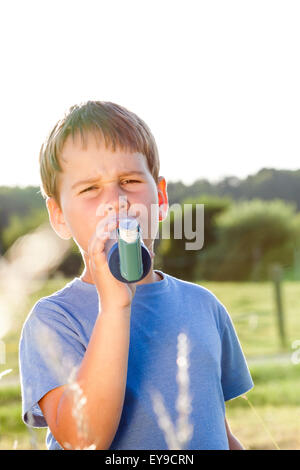 Boy utilizzando un inalatore per asma in villaggio con estate tramonto Foto Stock