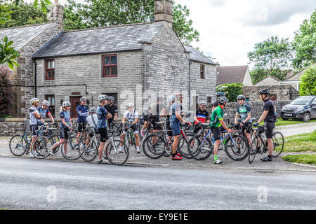 Un gruppo di ciclisti con le biciclette si incontrano sulla strada di fronte ad una scuola di pietra nel Peak District in procinto di prendere parte ad una gara Foto Stock