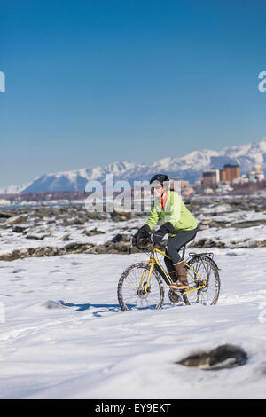 Una giovane donna corse pneumatici chiodati bicicletta accanto al Tony Knowles il sentiero costiero, Anchorage, centromeridionale Alaska, Stati Uniti d'America. Foto Stock