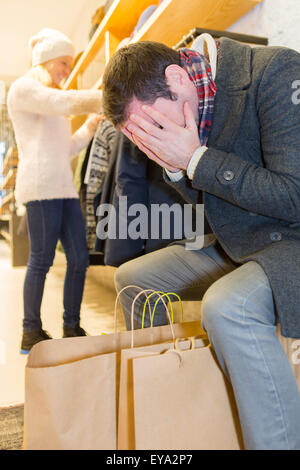 Vista di un giovane uomo informale in attesa mentre la moglie di shopping Foto Stock