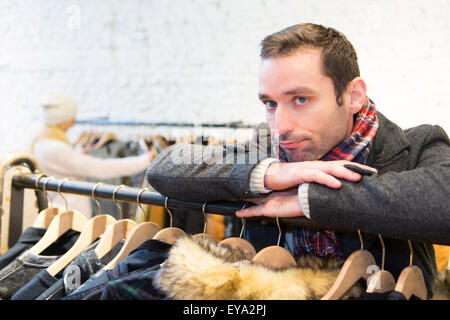 Vista di un giovane uomo informale in attesa mentre la moglie di shopping Foto Stock